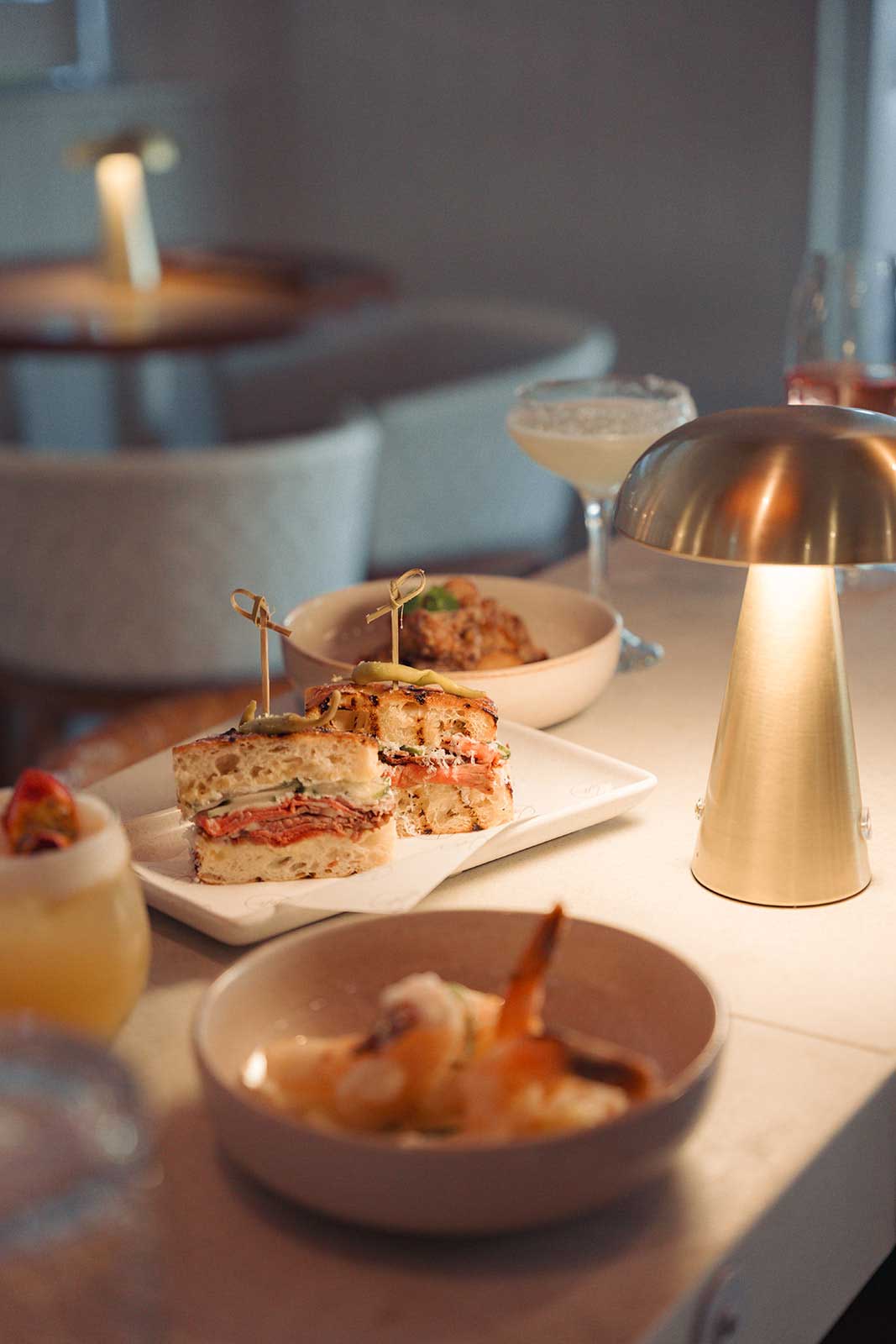 Loft Bar – Late Night Bar snacks and cocktails on a softly lit table beside a brass lamp at Loft Byron Bay